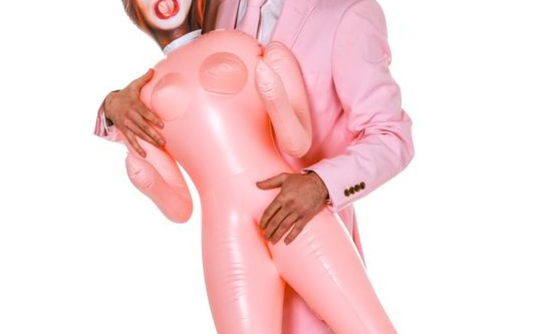A young man in a pink suit holding an inflatable doll on hist stag party